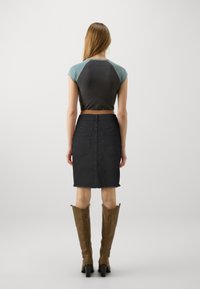 Svart denim blyantskjørt med rå kant, kombinert med en tettsittende, kortermet topp med fargeblokker. Brune støvler til kneet fullfører antrekket.