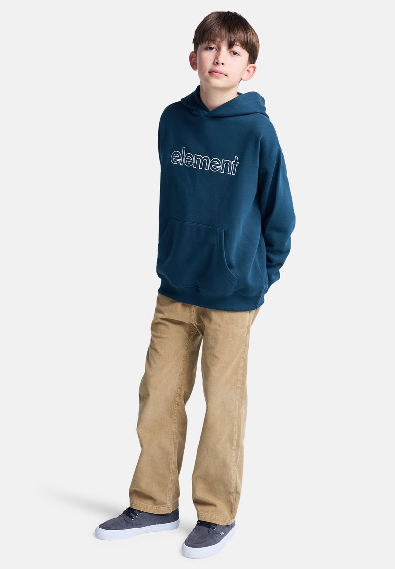 Barn står avslappet, iført en mørk blå hettegenser med "element" logo, beige bukser og grå sko, mot en ensfarget lys bakgrunn.