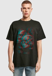 Schwarzes Baumwoll-T-Shirt mit einem grafischen Druck von sich überlappenden Schädeln in Türkis und Rot, umgeben von kreisförmigen dekorativen Elementen.