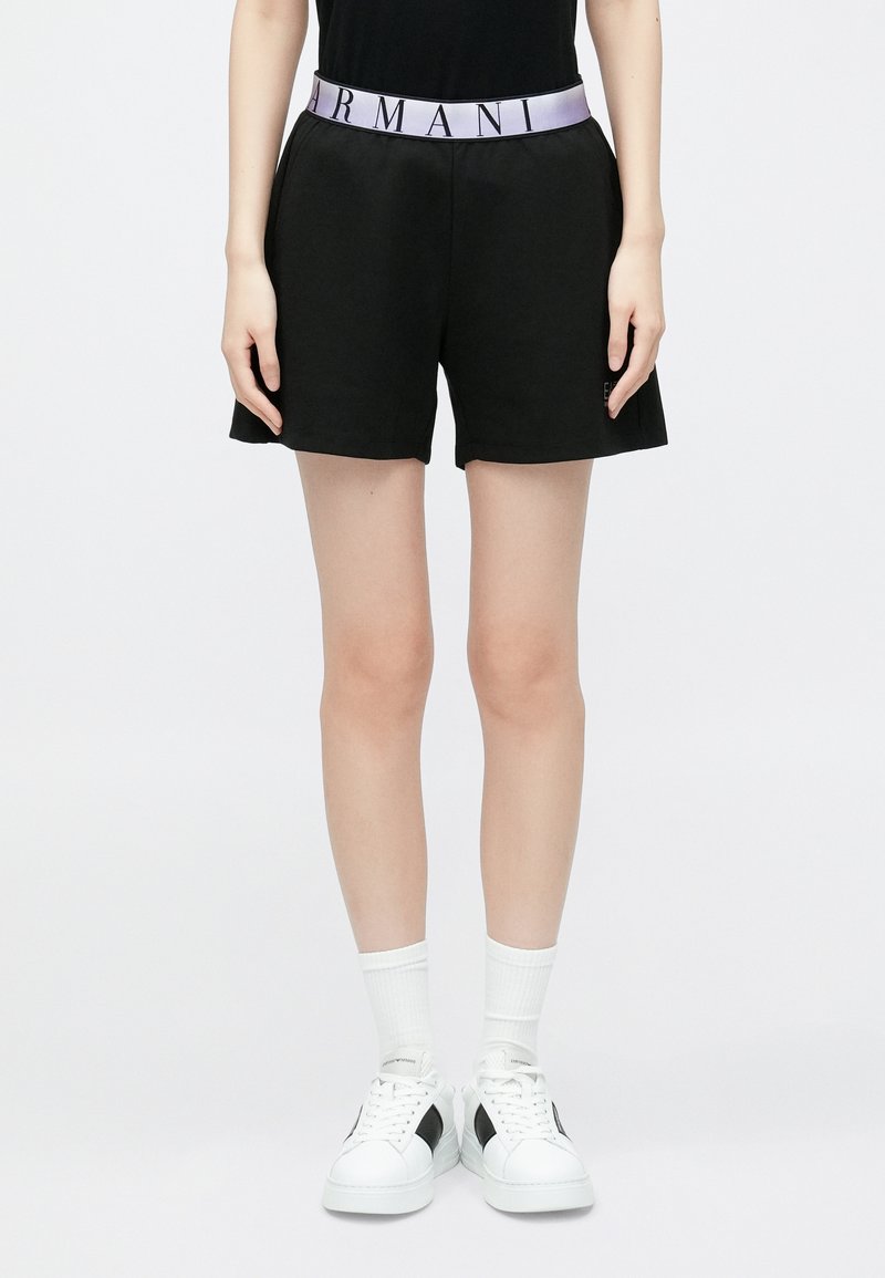 Pantaloni scurți negri cu talie elastică mov cu logo, potriviți liber și cu textură moale. Asortați cu adidași albi și șosete.