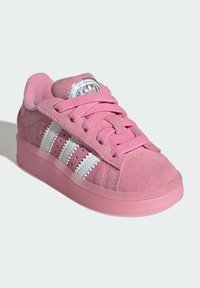 Child-sized pink suede sneaker with pink laces, white zigzag-striped sides, and a shiny logo on the tongue.