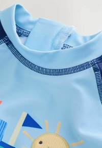 Costume da bagno azzurro chiaro con colletto alto, con disegni colorati di sole e barche a vela, e accenti blu scuro sulle spalle e sulle cuciture.