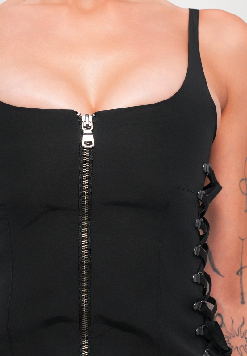 Zwart, aansluitend top met een centrale rits en zij-lace-up detail. Gladde stof met een gestructureerde vorm en verstelbare veters.