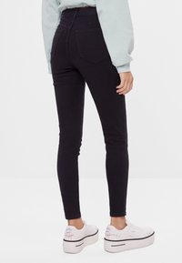 Svarta högmidjade skinny jeans med en texturerad yta, med två bakfickor och i kombination med kraftiga vita sneakers.
