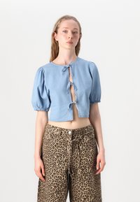 Ljusblå cropped denimblus med puffärmar och knytning fram, i kombination med bruna leopardmönstrade byxor med knappar.