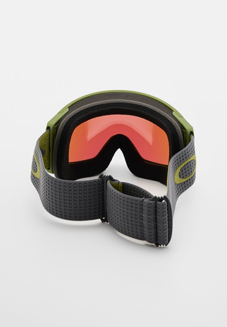 Gogle narciarskie z zieloną ramką i soczewkami o czerwonym zabarwieniu, z miękką pianką wypełniającą oraz teksturowanym szarym paskiem z regulowanymi klipsami.