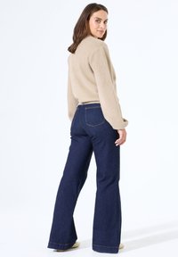 Beige, zachte, gestructureerde trui gecombineerd met donkerblauwe, wijde denim jeans met een hoge taille en zichtbare stiksels.