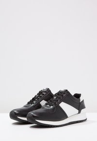 Černé kožené tenisky s bílým akcentem, kulatou gumovou špičkou, šněrovacím designem a texturovanou podrážkou pro lepší trakci.