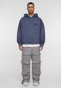 Navy blue hoodie with front pocket and logo, paired with gray cargo pants featuring multiple pockets and a relaxed fit. White sneakers.
