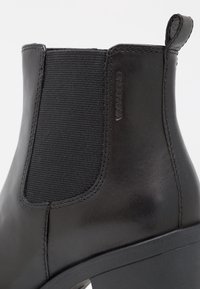 Zwarte enkelboots van glad leer met elastische zijpanelen, ronde neus en een hoge blokhak. "VAGABOND" logo in de zijkant gedrukt.