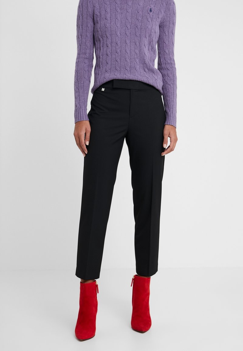 Svarta skräddarsydda byxor med en slät textur, kombinerade med en lila kabelstickad tröja och röda mockastövletter med gulddragkedjor.