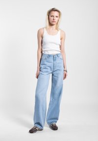 Lichtblauwe hoge taille jeans met een wijde pasvorm, gecombineerd met een aansluitend wit ribbel tanktop en donkerbruine veterschoenen.