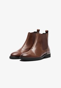 Botas Chelsea de cuero marrón con paneles elásticos en los lados, punta redonda y tiradores; superficie texturizada y suela de goma negra para mayor agarre.