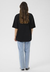 Juodas per didelis T-shirt su trumpomis rankovėmis, lygia tekstūra. Derinamas su šviesiai mėlynomis tiesiomis kelnėmis ir juodais basuotais batais su metaliniais akcentais.