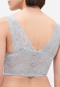 Mīksts zila mežģīņu bralette ar ziedu rakstu, plašām mežģīņu siksnām un viļņotu apakšmali. Aizmugurē dziļa V forma.