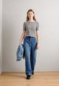 Juostuotas trumpas rankovėmis viršus, mėlyni platūs džinsai ir juodi batai. Modelis laiko šviesiai mėlyną džinsinį švarką. Sklandus tekstūros, laisvalaikio dizainas.