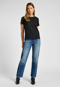 T-shirt nera in cotone a maniche corte, abbinata a jeans dritti blu chiaro con una striscia laterale scura, completata da stivaletti neri alla caviglia.