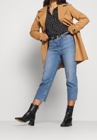 Béžový trenčkot přes černou blůzku s puntíky, ve spojení s vykrojenými modrými džíny a černými kotníkovými botami na podpatku. Značná třepená lem na džínech.