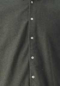 Dark green button-up shirt with a textured fabric, featuring a six-button placket and round, clear buttons. No visible patterns.
