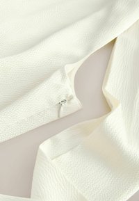 Tissu blanc texturé avec une petite tirette blanche partiellement dézippée sur une manchette de manche ou de jambe de pantalon.