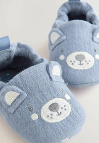 Pantofole di tessuto blu con design a faccia di orso, caratterizzate da dettagli ricamati, forma arrotondata e texture morbida. Aperture elastiche per una facile calzata.