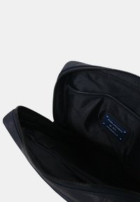 Marinblå læder clutchtaske med en glat overflade, lynlås lukning og indvendige lommer; har et mærketiket og minimalistisk design.
