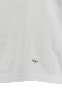 Camiseta de algodón blanca con una textura suave, que presenta una insignia ovalada plateada con el texto "Key Largo" cerca del dobladillo.