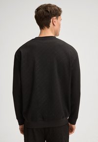 Felpa nera con motivo texture, scollo a girocollo e polsini a costine. La vista dal retro mostra una vestibilità rilassata e tessuto uniforme.