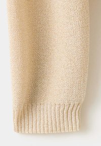 Gros plan d'une manche de pull beige tricoté montrant le poignet côtelé texturé et le motif de points tissés sur le tissu.