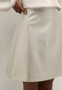 Egy krémszínű, selymes A-vonalú szoknya sima textúrával és térd feletti szegéllyel, amely egyszerű, letisztult dizájnnal rendelkezik.