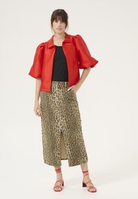 Veste courte en satin rouge avec des manches bouffantes, associée à une jupe à imprimé léopard avec une fente à l'avant. Le modèle porte des sandales rouges à lanières.