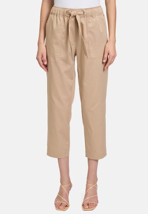 Beige cropped pants with an elastic waistband and tie, featuring two front pockets and a smooth cotton texture. Paired with strappy sandals.