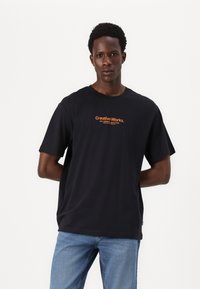 Kortærmet sort bomulds t-shirt med et fremtrædende orange logo print på fronten. Løst fit med en klassisk rund halsudskæring.