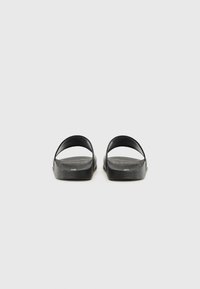 Svarta sandaler med öppen tå, slät textur, böjda remmar och platta sulor. Minimalistisk design, lämpliga för avslappnad användning.