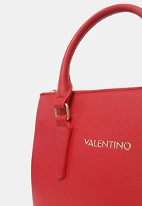 Borsa a tracolla rossa testurizzata con forma strutturata, logo dorato e manico superiore. Presenta una finitura liscia e dettagli di cucitura sottili.