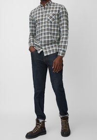 Karierte Button-Down-Bluse in Blau, Grün und Grau; mit einer Brusttasche und langen Ärmeln. Kombiniert mit dunklen Jeans und braunen Stiefeln.