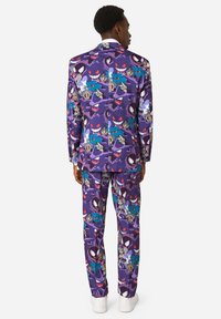 Fialový oblek s motívom rôznych kreslených postavičiek, vyrobený z hladkej látky. Obsahuje zladené nohavice a biele tenisky.