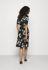 Czarna sukienka z krótkimi rękawami, ozdobiona białym kwiatowym wzorem. Rozkloszowany dół, wcięcie w talii, noszona z czarnymi sandałami na obcasie.