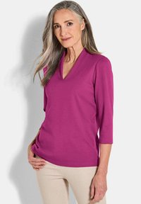 Fuchsia V-hals top met 3/4 mouwen, zachte textuur en een ontspannen pasvorm, gecombineerd met lichtbeige broeken. Geen zichtbare patronen of hardware.