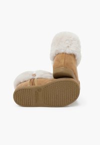 Botas de ante color arena con un grueso cuello de piel sintética blanca, suela de goma texturizada y detalles de costura expuesta. Diseño ligero y de altura hasta el tobillo.