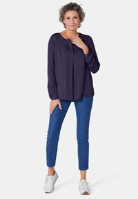 Camicia a maniche lunghe blu navy con scollatura a V e patta dei bottoni, abbinata a jeans skinny blu e sneakers bianche. Tessuto liscio, look casual.