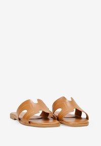 Sandali in pelle marrone con un design traforato, suola piatta, punta aperta e dettagli cuciti. Texture liscia con uno stile minimalista.