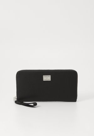 Portefeuille zippé noir fabriqué en matériau synthétique lisse. Présente une plaque logo en argent et un bracelet pour un transport pratique.