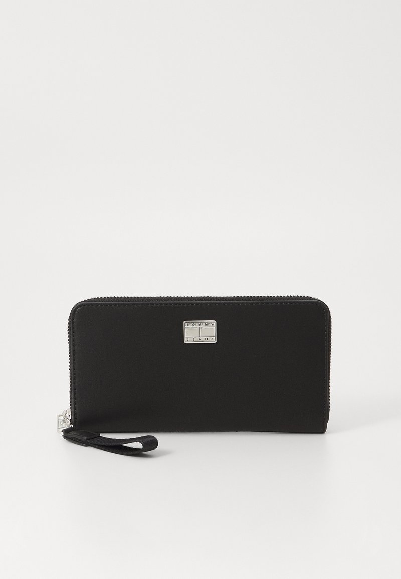 Portafoglio nero con zip fatto di materiale sintetico liscio. Presenta una placca con logo argentato e un manico per un facile trasporto.