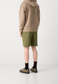 Felpa nera, pantaloni verdi, calze nere e sneakers oliva. L'outfit casual presenta un tessuto morbido e una vestibilità rilassata, con tasche laterali con zipper.