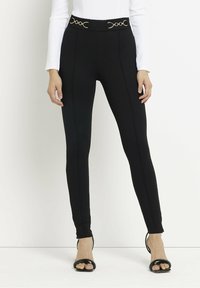 Zwarte leggings met een hoge tailleband voorzien van gouden cirkelvormige accenten, een gladde textuur, een nauwsluitend ontwerp en opvallende naaddetails.