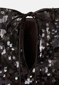 Tela negra con lentejuelas negras y plateadas, que presenta un escote con abertura en forma de llave atado con un lazo negro.