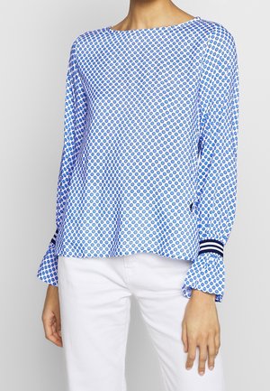 Blouse pull bleu et blanc avec un col rond, des manches longues avec des poignets froncés et un motif à pois sur l'ensemble.