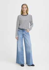 Chemise à manches longues rayée bleu marine et blanche, associée à un jean denim bleu clair à jambes larges et des bottines noires. Ceinture simple pour accentuer.
