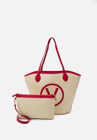 Stor beige axelväska med röda detaljer och en rund logo; i kombination med en mindre clutch, också beige med en röd dragkedja och rem.